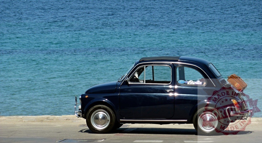 Fiat 500 vintage car preparing for Mediterranean road trip | Fiat 500 vintage car parked by the sea with a suitcase, ready for travel - Realisiert mit Pictrs.com