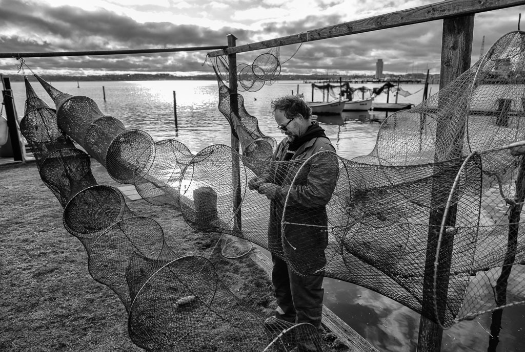fischer-2020-011 | Der Fischer Matthias Nanz aus Schleswig ist einer der letzten Berufsfischer an der Schlei. Die Fischerei war früher prägend für den Schleswiger Stadtteil Holm, in dem Matthias Nanz lebt. Das Bild zeigt ihn bei der Reparatur seiner Reusen. - Realisiert mit Pictrs.com