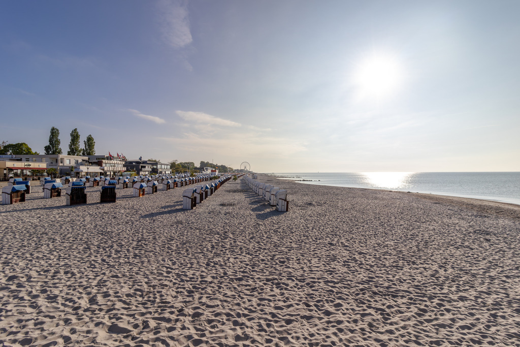 Wandbild: Morgenstimmung am Strand – Grömitz erwacht | Dieses Wandbild zeigt die friedliche Morgenstimmung am Strand von Grömitz. Die Sonne steht noch tief am Himmel und wirft lange Schatten über den feinen Sand. In geordneten Reihen stehen Strandkörbe bereit, ausgerichtet zum ruhigen Meer, das sich unter dem klaren Himmel bis zum Horizont erstreckt. Die Szene wirkt strukturiert und zugleich weitläufig – ein Moment der Stille, bevor der Tag beginnt. In der Ferne sind Gebäude und ein Riesenrad zu erkennen. Die Komposition verbindet natürliche Schönheit mit maritimer Infrastruktur und eignet sich ideal als Wandbild für ruhige, lichtdurchflutete Wohnkonzepte. Erhältlich als Leinwandbild, Acrylglasbild, Alu-Dibond FineArt Print oder als Akustikbild – ein stilvoller Akzent für Wohnzimmer, Büro oder Ferienwohnung. - Realisiert mit Pictrs.com