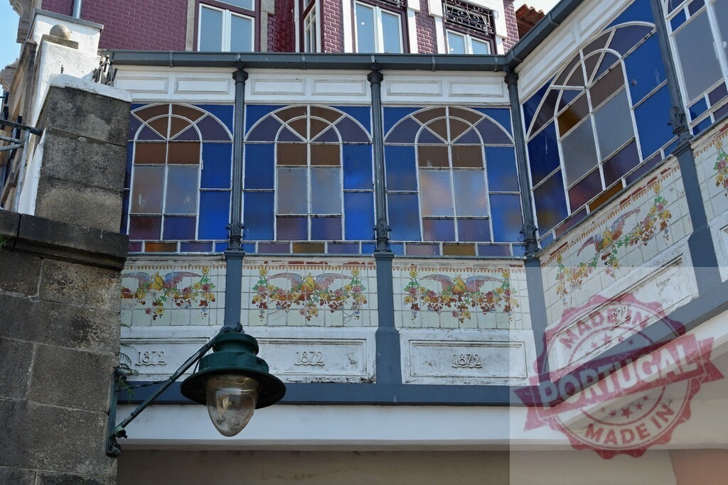 Old building facade with stained glass windows and street lantern. Porto - Portugal | Building facade displaying arched stained glass windows and decorative ceramic tiles with a vintage street lamp - Realized with Pictrs.com