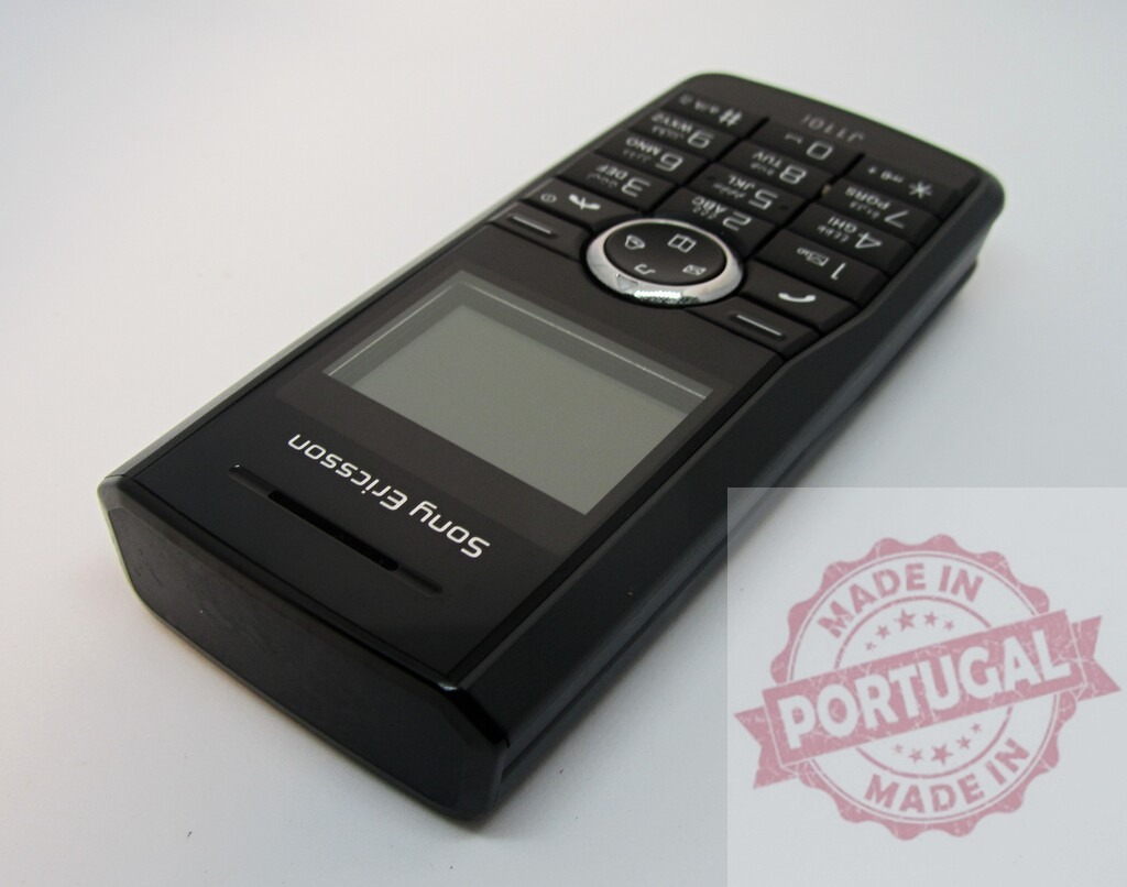 Black Sony Ericsson J110i cell phone lying on a white background | Sony Ericsson J110i mobile phone showing blank screen on white background - Realisiert mit Pictrs.com