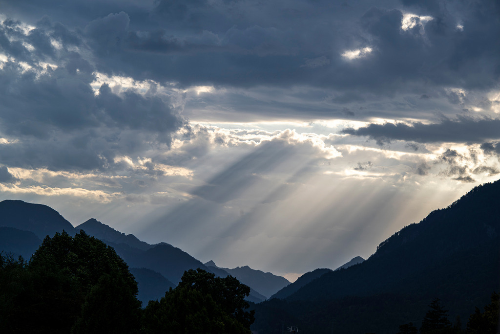 Himmelsleiter über den Gipfeln: Magischer Lichtzauber in den Alpen | Ein drama- und stimmungsvoller Naturmoment im Ammergebirge bei Garmisch-Partenkirchen: Durch eine dramatische, dunkle Wolkendecke brechen kraftvolle Sonnenstrahlen und tauchen das Bergpanorama in ein mystisches Licht. Die Silhouetten der Bergkämme zeichnen sich scharf ab, während die fächerförmigen Lichtstrahlen wie eine Himmelsleiter ins Tal hinabscheinen. Eine eindrucksvolle Aufnahme voller Ruhe, Ehrfurcht und der zeitlosen Faszination des oberbayerischen Alpennaturerlebnisses. - Realisiert mit Pictrs.com