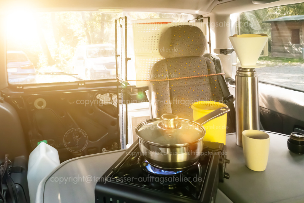Kaffee kochen im Van | Vanlife. Wasser wird auf einem Gaskocher gekocht. Kaffee wird zubereitet. Thermoskanne, Kaffeefilter Halter, Stielkasserolle stehen auf dem Tisch im Font eines Van auf einem Parkplatz.