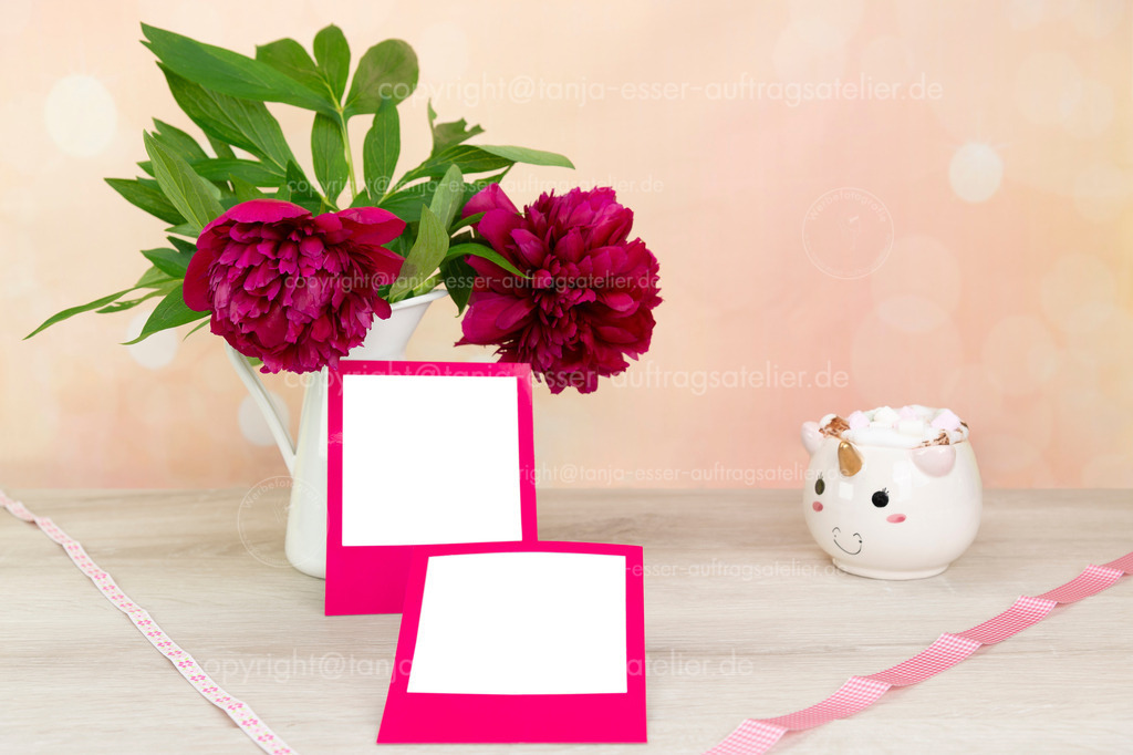 Bilderrahmen und Pfingstrose D | Mock Up für quadratische Flächen in pinkem Rahmen. Pfingstrosen (Paeonia) in einer weißen Blechvase. Eine Einhorntasse mit Marshmallows. Heller Hintergrund in Pfirsich- und Rosatönen mit Bokeh. Holzuntergrund und Copy Space.