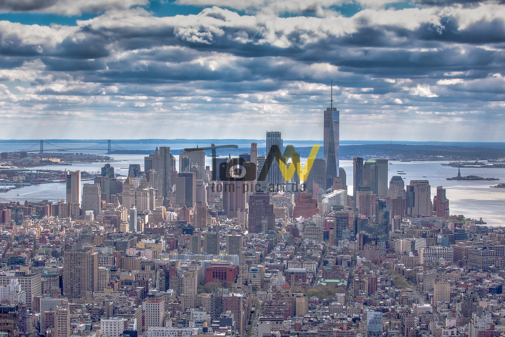 Skyline von New York mit One World Trade Center---Panorama | Die Abbildung zeigt eine Luftaufnahme der Skyline von Lower Manhattan, New York City. Im Zentrum des Bildes sind mehrere markante Gebäude und Sehenswürdigkeiten zu erkennen: Das höchste und prominenteste Gebäude im Zentrum der Skyline ist das One World Trade Center (auch Freedom Tower genannt).In der Ferne, auf der rechten Seite, ist die Freiheitsstatue in der Upper New York Bay zu sehen.Das Gebiet umfasst das Finanzviertel von Manhattan, bekannt für seine dichte Bebauung mit Wolkenkratzern. - Realisiert mit Pictrs.com