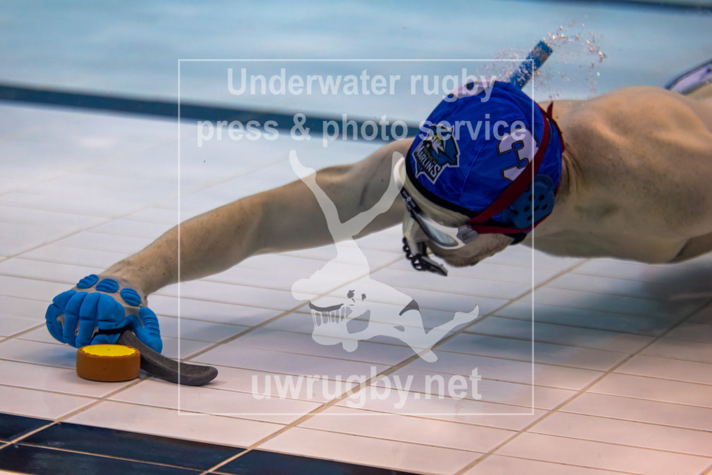 Unterwasser-Hockey: Rückrunde Liga 2023/2024 - Bild 9 | Spieler der München Marlins spiel den Puck durch das Spielfeld. Seine Hand mit dem Schläger ist mit einem Schutzandschuh gegen Schläge durch gegnerische Sticks geschützt. - Realisiert mit Pictrs.com