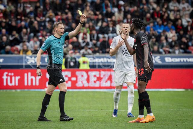 German Bundesliga, Bayer 04 Leverkusen vs. VfL Wolfsburg, 04.04.2026 | LEVERKUSEN, GERMANY - APRIL 4, 2026 :  referee Martin Petersen (Stuttgart) is showing Edmond Tapsoba (Bayer 04 Leverkusen, 12) a yellow card after a foul in the box causing a penalty, Denis Vavro (VfL Wolfsburg, 3) in the background during the German Bundesliga match on gameday 28 between Bayer 04 Leverkusen vs. VfL Wolfsburg at BayArena on April 4, 2026 in Leverkusen, Germany. DFL REGULATIONS PROHIBIT ANY USE OF PHOTOGRAPHS AS IMAGE SEQUENCES AND/OR QUASI-VIDEO.
