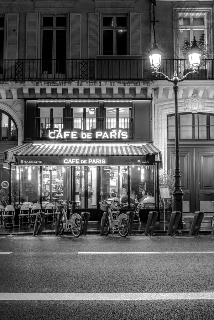 Parisian Glow | A quiet evening at a Paris café, where the glow of streetlights meets the warmth of conversation. In black and white, every reflection tells a story of timeless charm and urban poetry. - Realisiert mit Pictrs.com
