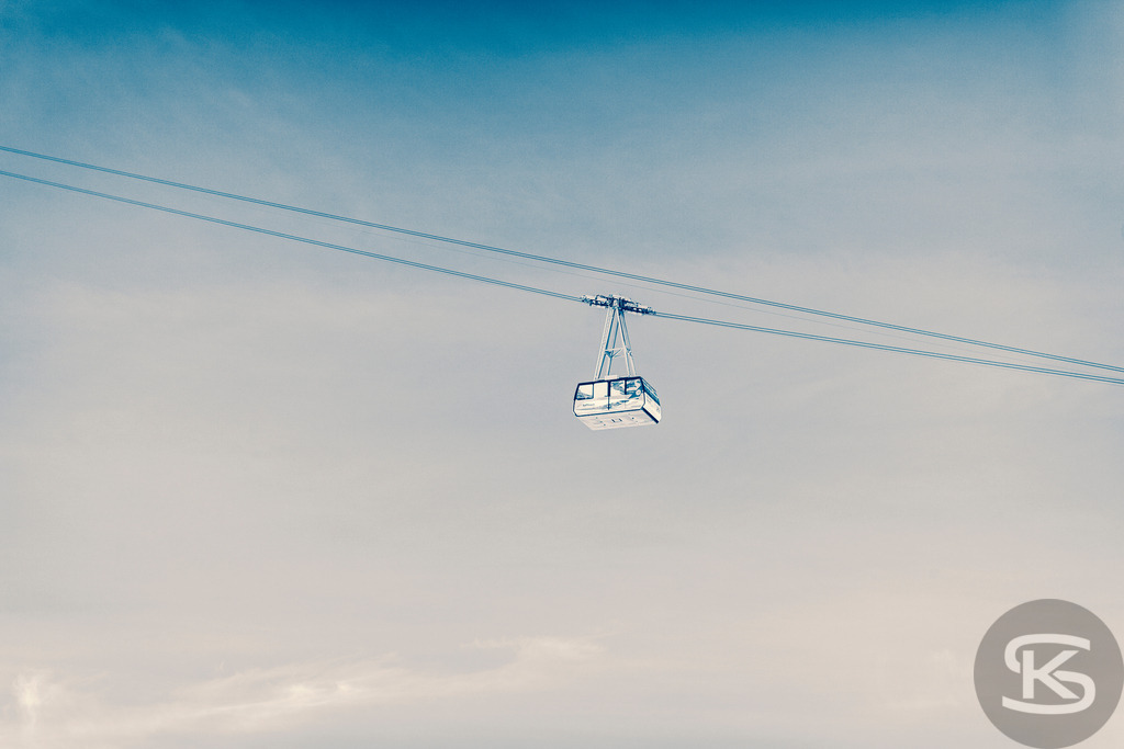 Gondelbahn über den Wolken, Wintersportregion Zugspitze | Eine Gondel einer Seilbahn schwebt hoch über einer dichten Wolkendecke, die die Berglandschaft verbirgt. Das Bild vermittelt ein Gefühl von Höhe, Ruhe und Abenteuer im Wintersportgebiet Zugspitze. Es zeigt die moderne Infrastruktur, die Skifahrer schnell in höhere Lagen bringt, oft oberhalb des schlechten Wetters im Tal. - Realisiert mit Pictrs.com