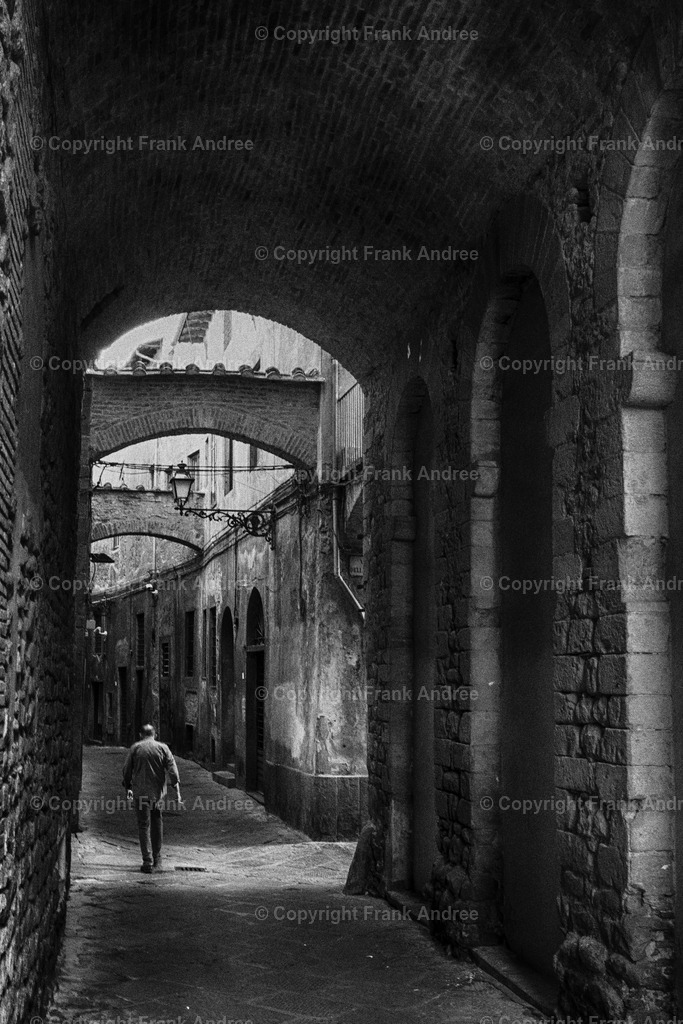 Pistoia 2 | Ein Mann geht allein durch eine enge Gasse in der Altstadt von Pistoia Toskana. Street photography aus Italien in schwarz weiß - Realisiert mit Pictrs.com