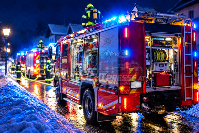 Feuerwehreinsatz bei winterlichen Bedingungen | Symbolbild eines nächtlichen Feuerwehreinsatzes bei winterlichen Bedingungen. Mehrere Feuerwehrfahrzeuge stehen auf einer schneebedeckten Straße und beleuchten die Umgebung mit Blaulicht und Einsatzbeleuchtung. Feuerwehrkräfte in Einsatzbekleidung sind bei den Fahrzeugen zu sehen. Das Bild dient als allgemeines Symbolfoto für Berichte über Feuerwehreinsätze, technische Hilfeleistungen und Einsätze bei winterlichen Straßenverhältnissen. Das Bild wurde bei einem Einsatz erstellt und danach mit KI optimiert. - Realisiert mit Pictrs.com