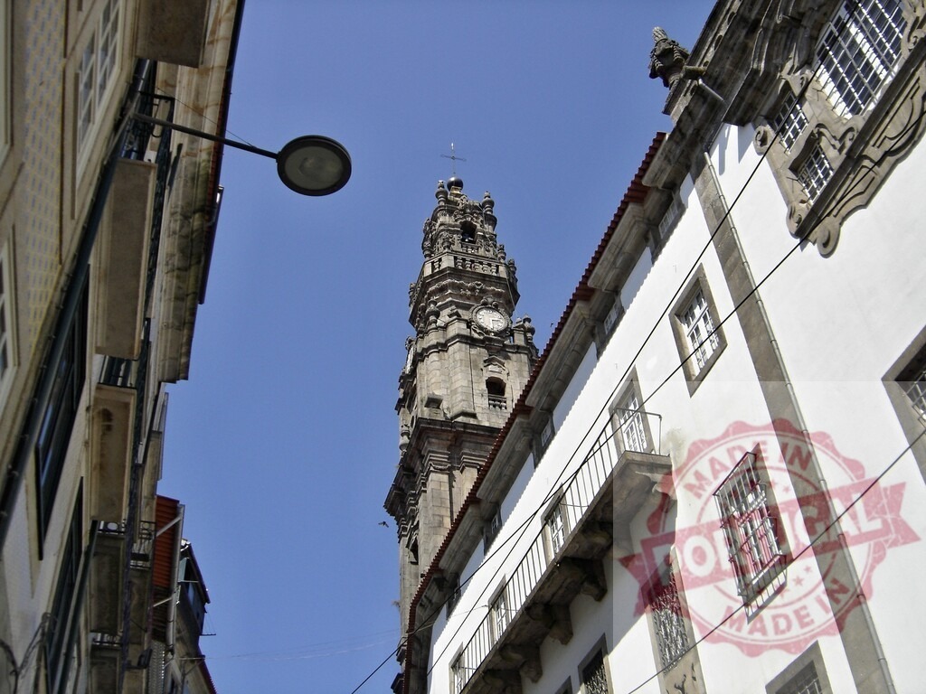 Clérigos Tower rising above historical buildings in Porto. Porto - Portugal | Clérigos Tower standing tall against a blue sky, viewed from a narrow street in Porto - Realized with Pictrs.com