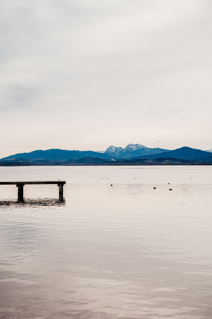 ein Morgen am See | Ein stiller Morgen am See mit einem Steg im Vordergrund und majestätischen Alpen im Hintergrund – ein atmosphärisches Fotokunstwerk voller Ruhe, Weite und natürlicher Schönheit. Ideal als Kunstdruck für inspirierende Räume. - Realisiert mit Pictrs.com