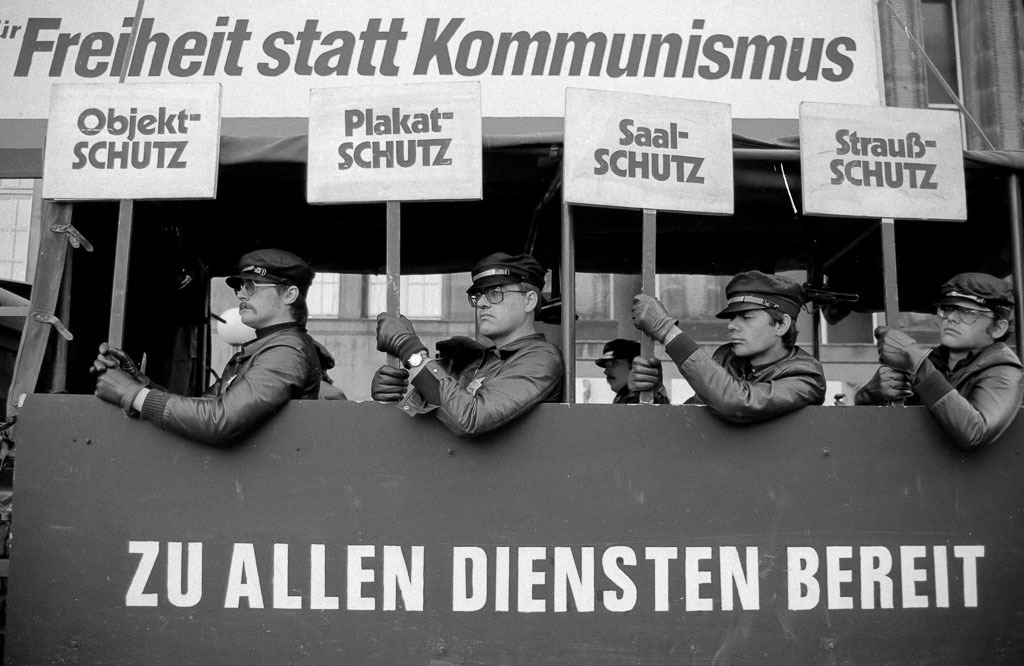 018-2017-01-14-0004 | Der Anachronistische Zug war ein politisches Straßentheater, das auf dem 1947 entstandenen gleichnamigen Gedicht von Bertolt Brecht basierte. Der Straßentheaterzug formierte sich 1980 in München als Protest gegen den damaligen Kanzlerkandidaten der CDU/CSU, Franz Josef Strauß, und präsentierte sich in mehreren deutschen Städten. Im September 1980 erreichte der Zug den Rathausmarkt in Kiel, wo dieses Szenenfoto entstand. - Realisiert mit Pictrs.com