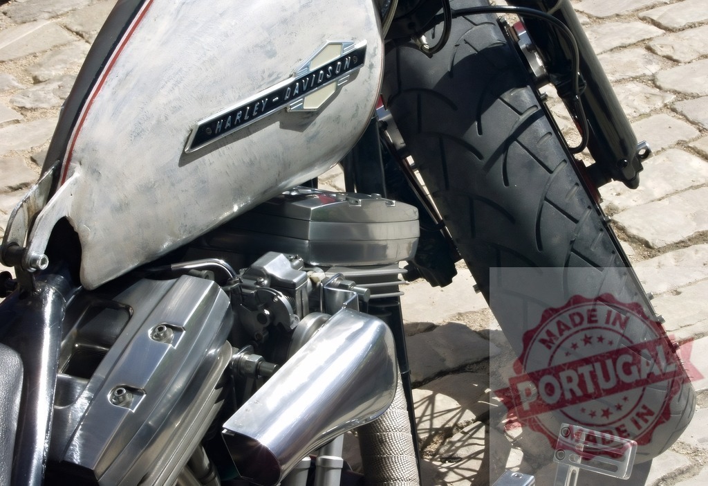Custom Harley-Davidson motorcycle engine, tank, and tire on cobblestone | Fuel tank, engine details, and front tire of a vintage custom Harley-Davidson motorcycle parked on a cobblestone street - Realisiert mit Pictrs.com