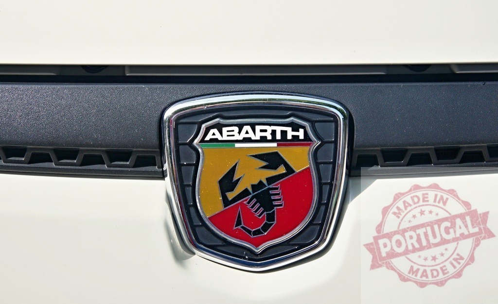 Abarth logo shining on a white car grill | Close-up of the Abarth logo, featuring a scorpion, displayed on the front grill of a white car - Realized with Pictrs.com