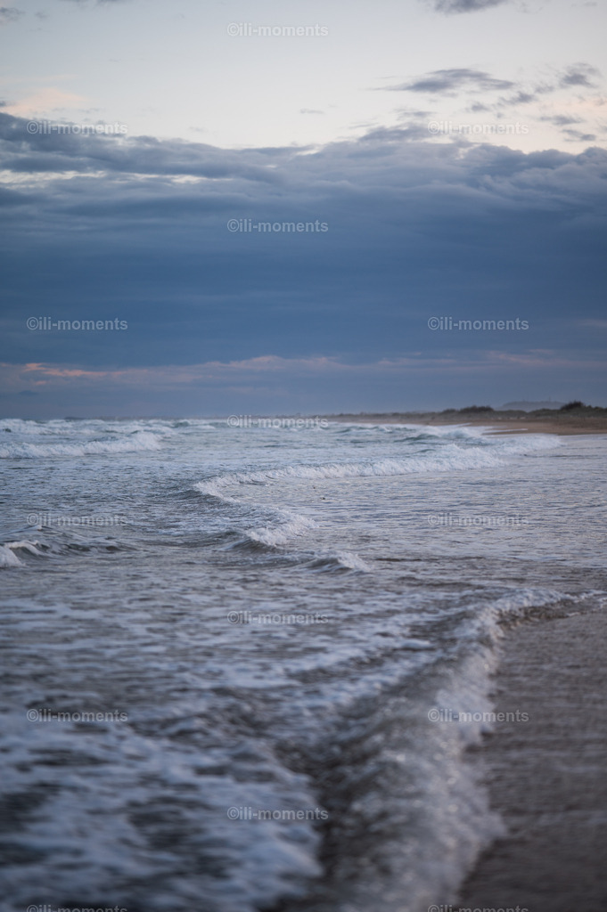 Wellen am Strand | Leicht stürmische Wellen schlagen am Strand ans Ufer, während ein bedeckter Himmel die Szene in ruhige, mystische Stimmung taucht. Ein kraftvolles Fotokunstwerk – ideal als Kunstdruck für naturverbundene Räume. - Realisiert mit Pictrs.com