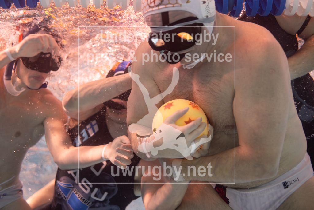 24. - 26.11.2023: Unterwasser-Rugby Champions Cup 2023  | HäSu (Hämeenlinna / Finnland) in blau gegen PF České Budějovice (Budweis / Tschechien) in weiß. Tomáš Rys (weiß #44) versucht den Ball erfolglos im Spielfeld zu halten, während ihn die finnischen Gegenspieler über die Seitenauslinie drücken. Da ein tschechischer Spieler den Ball in Ballbesitz war, bekommt Finnland Freiwurf. - Realisiert mit Pictrs.com