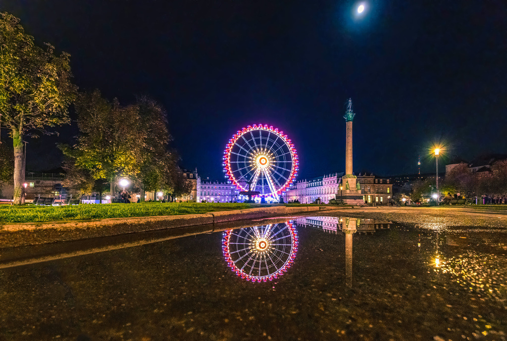 Das beleuchtete Riesenrad auf dem Schlossplatz in Stuttgart bei Nacht | Das Bild zeigt den Stuttgarter Schlossplatz bei Nacht, auf dem das Riesenrad „Sky Lounge Wheel“ vor der Jubiläumssäule und dem Neuen Schloss steht. Details zum Standort und den AttraktionenWahrzeichen: Im Vordergrund ist die Jubiläumssäule zu sehen, die zu Ehren von König Wilhelm I. errichtet wurde. Dahinter befindet sich das Neue Schloss, in dessen Ehrenhof das Riesenrad während der Wintermonate aufgestellt wird.Das Riesenrad: Es handelt sich oft um das „Sky Lounge Wheel“ des Betreibers Oscar Bruch jr.. Es hat eine Höhe von etwa 58 bis 60 Metern und verfügt über 40 Gondeln.Veranstaltungen: Das Riesenrad ist Teil der winterlichen Attraktionen in der Stuttgarter Innenstadt, oft im Zusammenhang mit dem Stuttgarter Weihnachtsmarkt oder den „Glanzlichtern Stuttgart“.  - Realisiert mit Pictrs.com