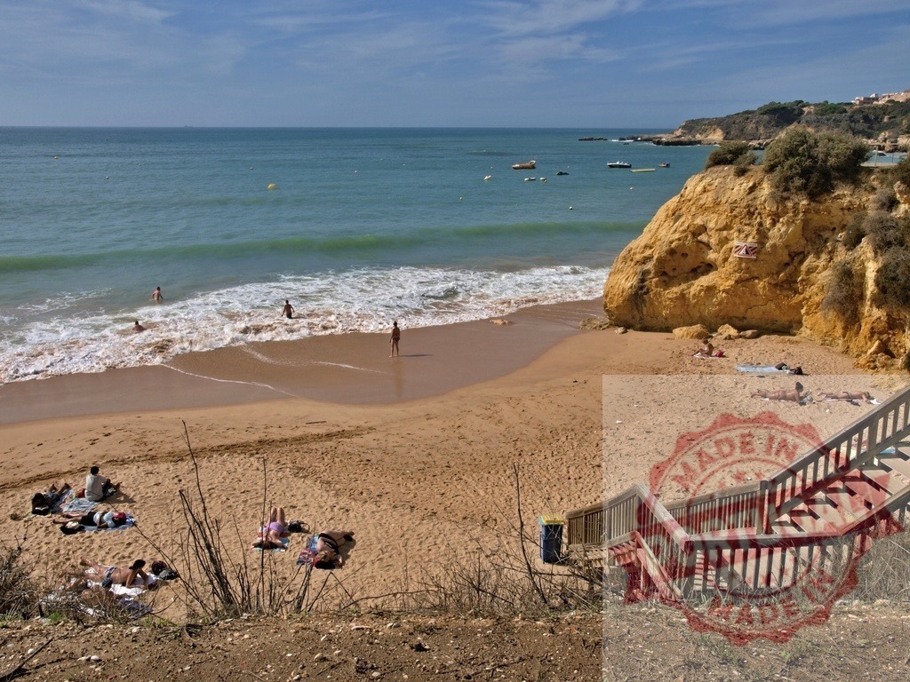 Sunny beach day in Algarve with ocean and cliff | People swimming in ocean waves and sunbathing on a sandy beach next to a golden cliff - Realisiert mit Pictrs.com