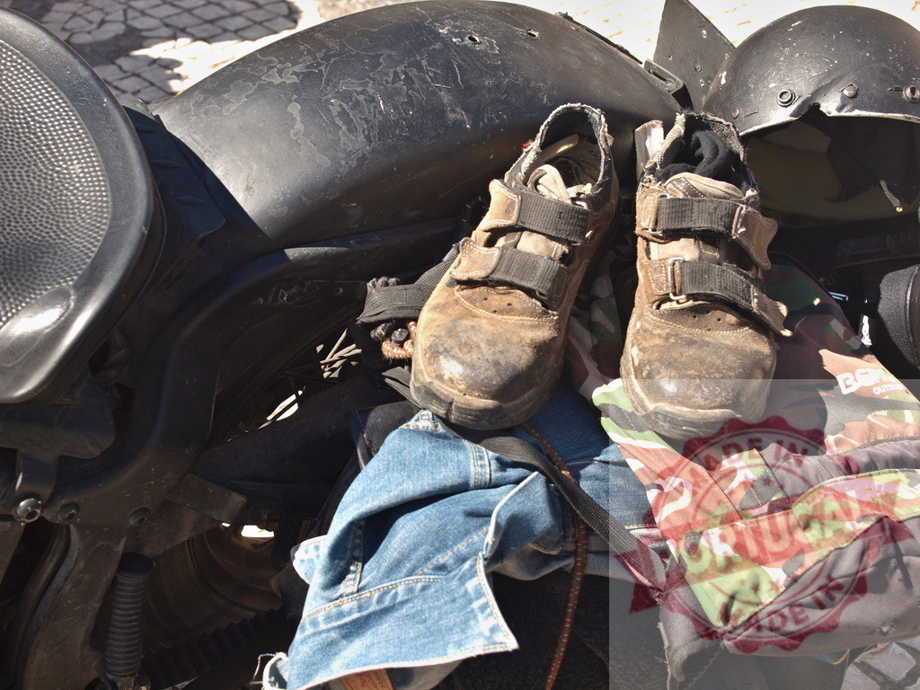 Motorcycle gear after a long journey adventure travel | Worn work boots, denim jacket, and camouflage bag resting on a black motorcycle tank - Realisiert mit Pictrs.com