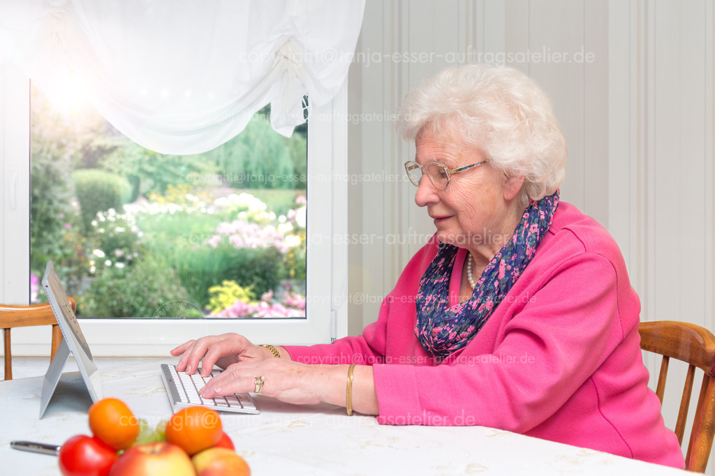 Alte Frau sitzt am Mini PC 2 D | 80 Jahre alte Frau, die allein zu Hause sitzt. Sie gehört zu der Risikogruppe für Covid 19. Die Seniorin schreibt am Tablet-PC gegen die Isolation mit ihrer Familie.