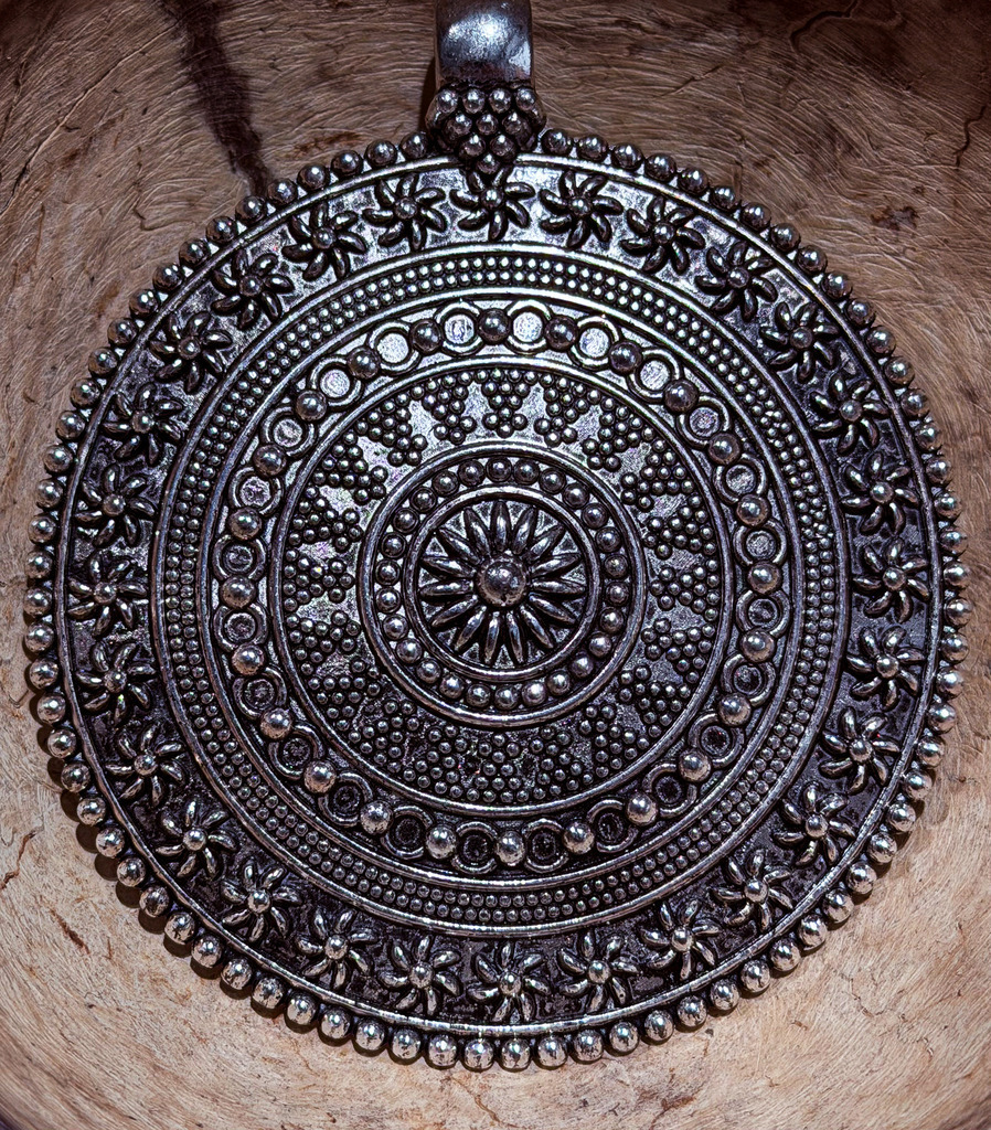 Silbernes Mandala: Metalldetails auf rustikalem Holz | Ein meisterhaftes Zusammenspiel aus metallischer Präzision und rustikaler Wärme. Diese detailreiche Makroaufnahme fängt ein filigranes, silbernes Metall-Ornament auf einer lebendig gemaserten Holzoberfläche ein. Die hypnotisierende Symmetrie des runden Mandalas zieht den Betrachter sofort in den Bann, während die plastische Struktur des Metalls für eine spürbare Tiefe sorgt. Dieses Kunstwerk verbindet eleganten Industrial-Chic mit natürlicher Gemütlichkeit. Besonders empfohlen als matter Alu-Dibond-Print, der den metallischen Charakter des Ornaments perfekt unterstreicht und Reflexionen im Raum minimiert. - Realisiert mit Pictrs.com