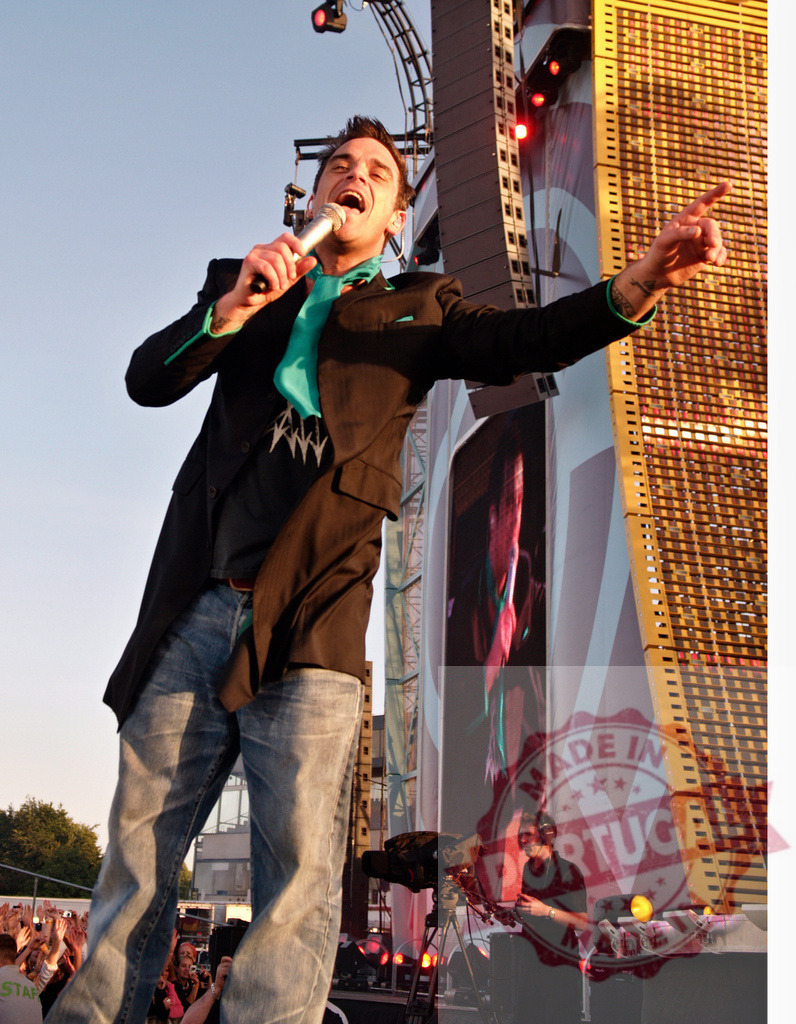 Robbie Williams singing and performing during a live concert | Robbie Williams entertaining crowd, singing with microphone and gesturing on stage during a live concert - Realisiert mit Pictrs.com