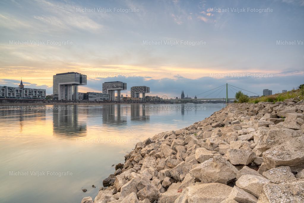 Am Rheinufer in Köln | Blick von den Pollerwiesen in Richtung Kranhäuser und Kölner Dom im Hintergrund. Der Rhein führt sehr wenig Wasser, bei Normalpegel sind die Steine komplett vom Wasser bedeckt. Die Gebäude der Kölner Skyline spiegeln sich im relativ ruhigen Wasser. - Realisiert mit Pictrs.com