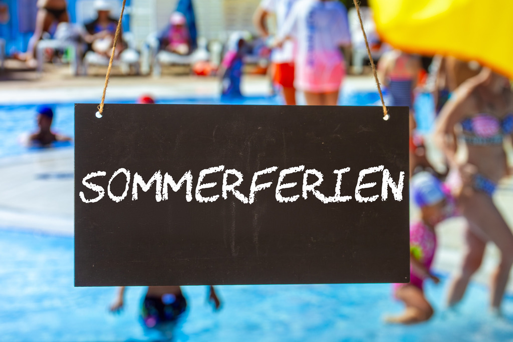 Sommerferien Schild | Symbolbild Sommerferien: Schild mit der Aufschrift SOMMERFERIEN vor Sommerurlaubern im Freibad (Composing) - Realisiert mit Pictrs.com