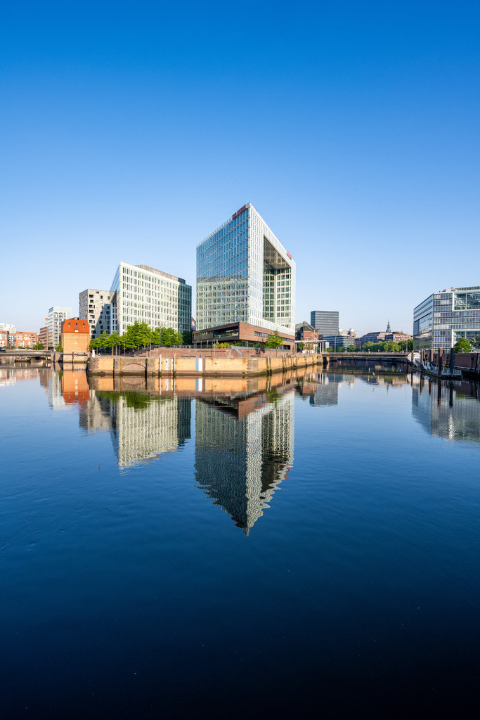 Moderne Architektur in der HafenCity | Minimalistische Aufnahme moderner Architektur in der Hamburger HafenCity mit ruhiger Wasserfläche und klarer Spiegelung. - Realisiert mit Pictrs.com