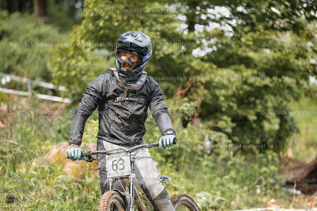 Trial-Fahrer in Aktion | Ein Mann in voller Ausrüstung fährt auf einem Gelände mit einem Motorrad. Er trägt einen schwarzen Helm, eine schwarze Jacke und Handschuhe. Er trägt eine Nummer 63 auf dem Motorrad. - Realisiert mit Pictrs.com