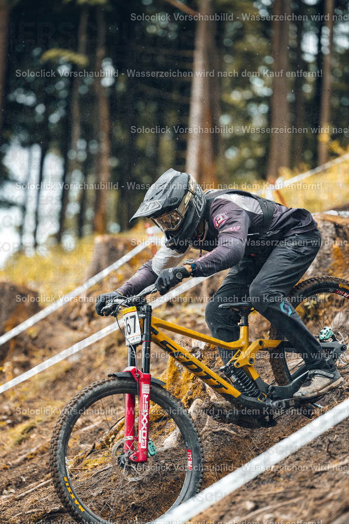 Mountainbike-Action im Wald | Das Bild zeigt einen Mountainbiker in voller Montur, der einen steilen, mit Wurzeln und Steinen übersäten Hang hinunterfährt. Er ist in einer dynamischen Position, bereit für einen Sprung. Der Fokus liegt auf dem Fahrer und seinem Mountainbike, wobei der Hintergrund aus dichtem, grünen Wald besteht. - Realisiert mit Pictrs.com