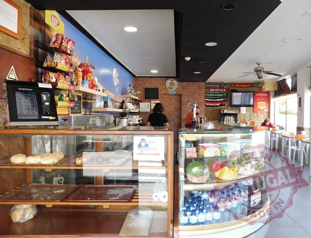 Cafe interior with counter displaying food and drinks | Cafe interior showing a food display counter, snacks, drinks, and a seating area - Realisiert mit Pictrs.com