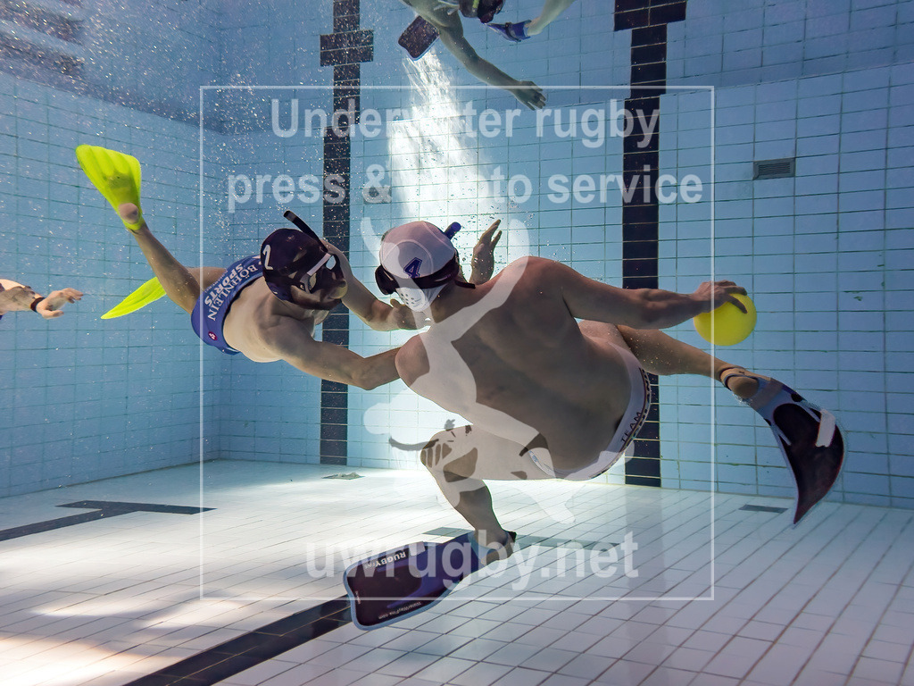 Spielsituation in der Spielfeldmitte | In der Mitte des Unterwasserrugby Spielfeldes versucht der blaue Stürmer den ballführenden weißen Angreifer zu stoppen.  - Realisiert mit Pictrs.com