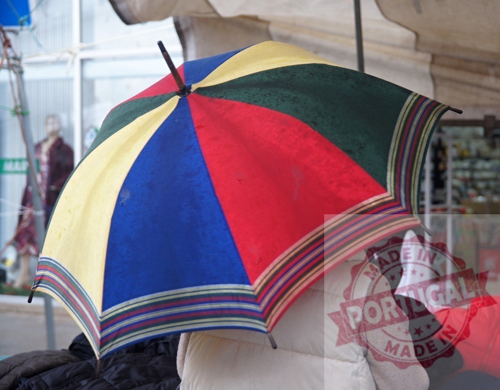 Person holding multicolored umbrella at street market | Person holds colorful umbrella protecting from weather at an outdoor market - Realisiert mit Pictrs.com