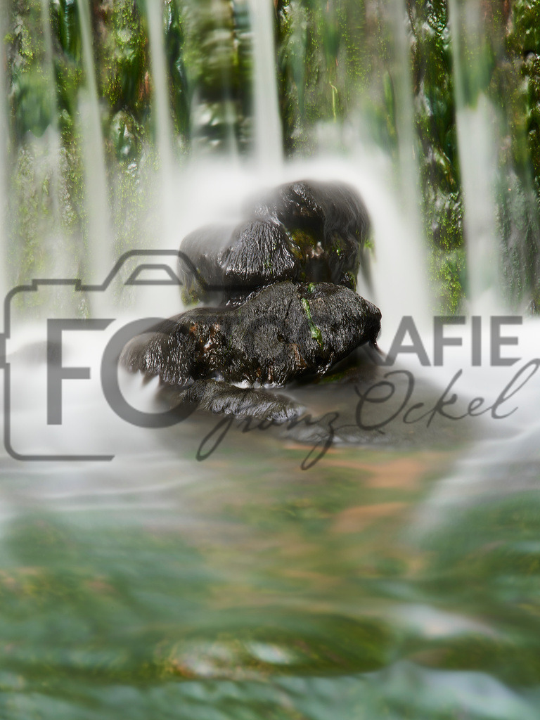 Fels in der Brandung | Im grün bemoosten Flussbett bei Aura (UFr) wird ein Steinstoß vom Wasserfall umspült. - Realisiert mit Pictrs.com