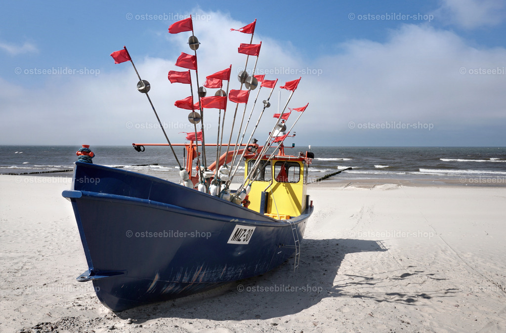 Blaugelber Fischkutter am Ostseestrand | Ein Fischkutter liegt bei Misdroy mit wehenden Netzflaggen am Strand. Im Hintergrund ist die Ostseebrandung zu sehen.