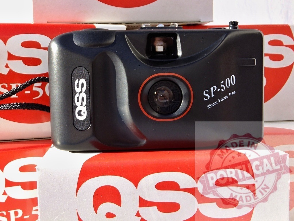 QSS SP-500 35mm point-and-shoot camera on packaging | Black QSS SP-500 point-and-shoot film camera resting on red and white branded boxes - Realisiert mit Pictrs.com