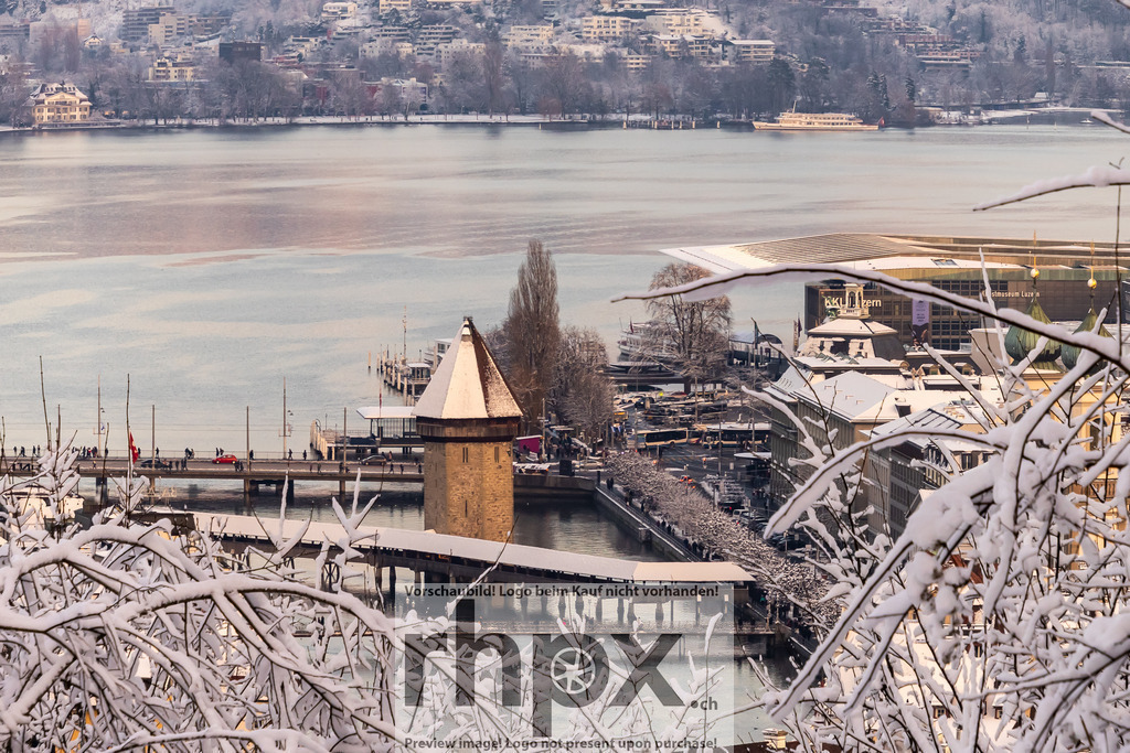Kapellbrücke Luzern im Winter | Stadt. See. Winterkleid. Der Blick gleitet durch tief verschneite Zweige hinab auf die Kapellbrücke und das weite Seebecken vor dem KKL. Die weisse Pracht auf den Dächern und Bäumen verwandelt die geschäftige Stadt in eine gedämpfte, harmonische Winterlandschaft. Wähle unter "Produktauswahl" dein Wunschformat: Vom klassischen Wandbild über Puzzle &amp; Tassen bis zum digitalen Download (z.B. als Handy-Hintergrund). - Realisiert mit Pictrs.com