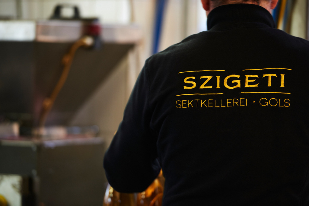 Sektkellerei Szigeti | Gols, Austria - February 19, 2018: Sektkellerei Szigeti; Mitarbeiter am Arbeitsplatz mit schwarzer Jacke und goldener Szigeti Aufschrift. - Realisiert mit Pictrs.com