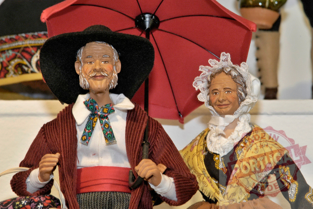 Elderly couple figurines holding a red umbrella | Two figurines of an elderly couple, dressed in traditional clothes, holding a red umbrella - Realized with Pictrs.com