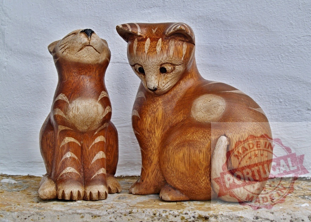 Wooden cat statues looking up and looking down | Wooden cat statues displaying unique carved poses on a textured surface - Realized with Pictrs.com