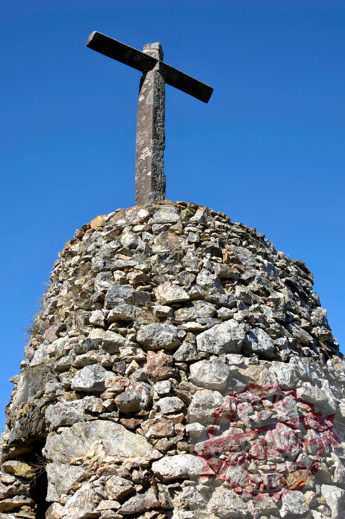 Stone cross monument on a cairn reaching into blue sky | Stone cross standing on a cairn reaching into a clear blue sky, symbolizing faith and remembrance - Realisiert mit Pictrs.com