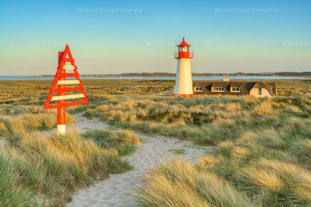 Leuchtturm List-West im Abendlicht | Blick zum Leuchtturm List-West auf der Nordseeinsel Sylt. Die Abendsonne taucht die Szene in ein schönes, warmes Licht. Links im Bild ist eine Tagmarke zu sehen, welche von See aus gesehen die Grenzlinie zwischen Dänemark und Deutschland markiert. - Realisiert mit Pictrs.com