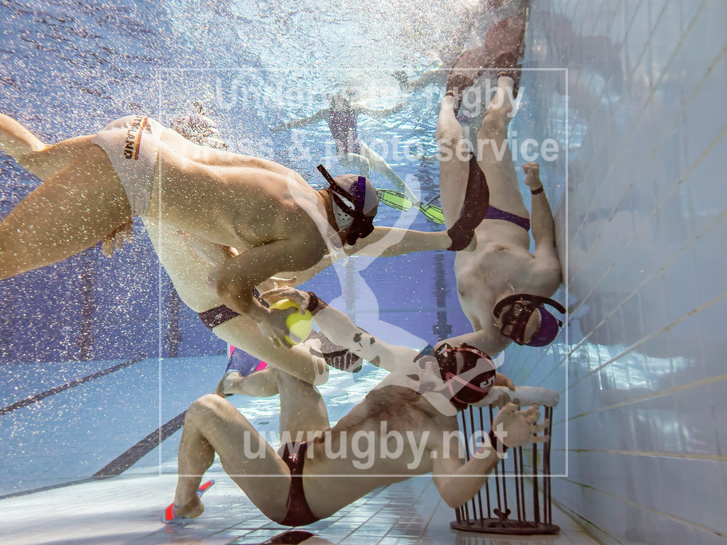 Angriff auf das Tor der blauen Unterwasser-Rugby Mannschaft | Der weiße Angreifer erkennt die Lücke in der blauen Verteidigung und versucht den Verteidiger zu überwinden, um den Ball in das gegnerische, noch offene, Tor abzulegen. Jedoch kommt der blaue Torwart noch im richtigen Moment um sich auf das eigene Tor zu legen und den Angriff der weißen Mannschaft zu erschweren.  - Realisiert mit Pictrs.com