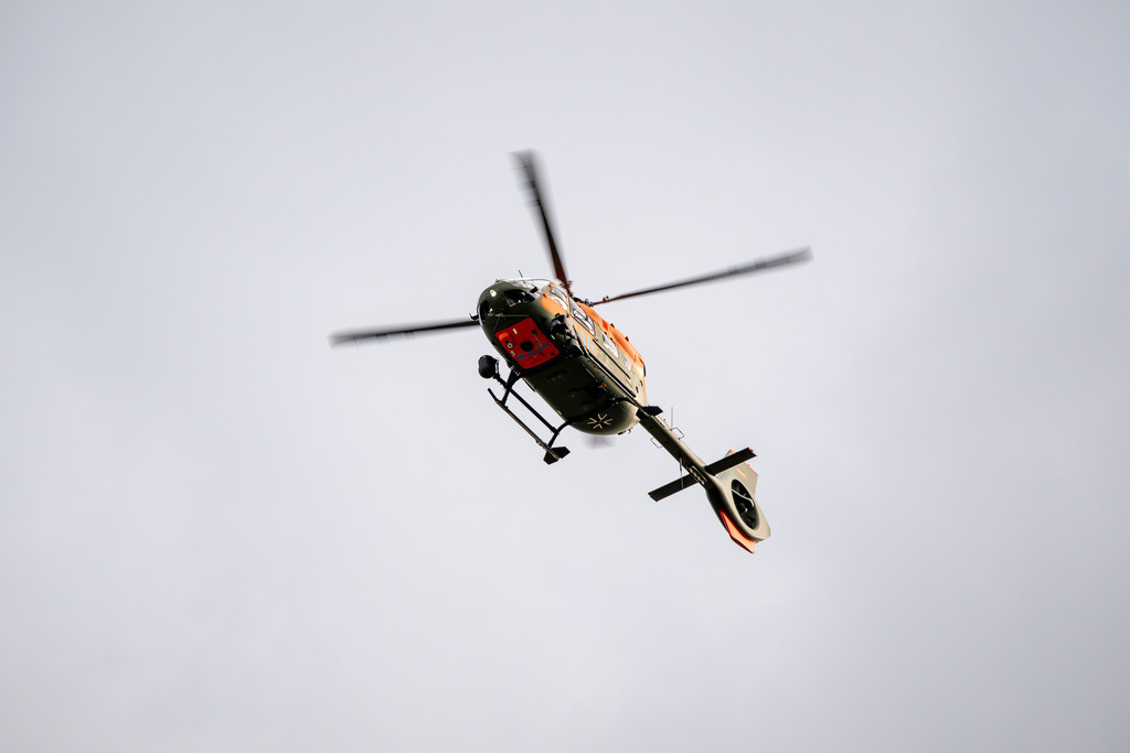 Airbus H145 LUH SAR Hubschrauber  | Die Aufnahme zeigt einen Airbus H145 LUH SAR Hubschrauber der Bundeswehr in der Untersicht gegen einen klaren, blauen Himmel. Der Helikopter ist in olivgrün und leuchtendem Orange (Dayglow) lackiert, trägt die Aufschrift „SAR“ (Search and Rescue) sowie das Eiserne Kreuz und verfügt über einen markanten Fenestron-Heckrotor. - Realisiert mit Pictrs.com