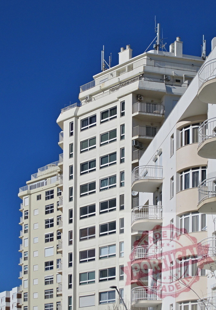 Modern residential urban buildings reaching blue sky. Algarve - Silves | Modern residential buildings with balconies and windows standing tall against a clear blue sky - Realized with Pictrs.com