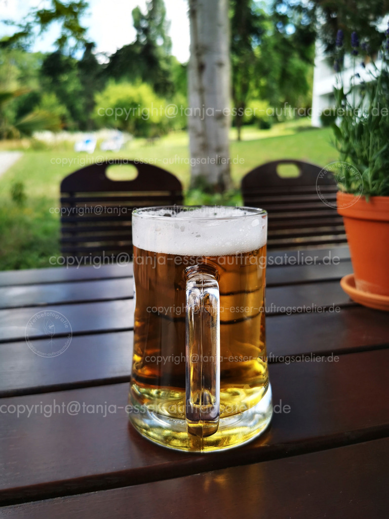Bier im Biergarten D | Im Sommer steht ein großes halber Liter Glas Bier auf einem Tisch in einem Biergarten. Im Hintergrund ist grüne Natur zu sehen. 