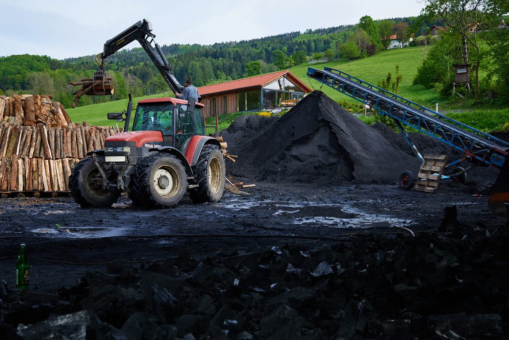 Waldköhlerei Hochecker | Michelbach, Austria - May 08, 2019: Waldköhlerei Hochecker, die 2011 in das Nationale Verzeichnis des immateriellen Kulturerbes der UNESCO aufgenommen wurde, produziert noch echte Holzkohle; roter Traktor mit Holzkran beim Aufbau des Kohlmeilers. - Realisiert mit Pictrs.com